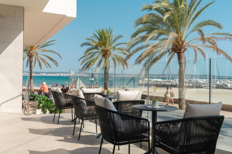 Terraza exterior con sillas y mesas del Hotel Las Arenas con vistas a la playa y palmeras