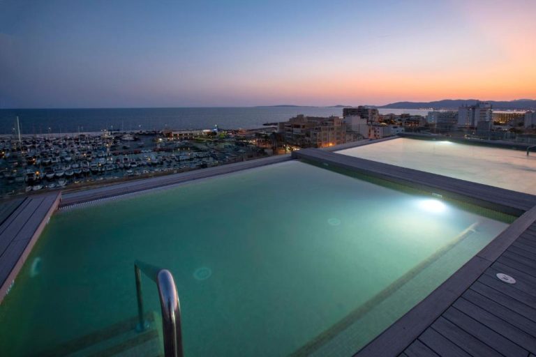 Piscina infinita en la azotea del Hotel Las Arenas con vistas al puerto deportivo y al mar al atardecer