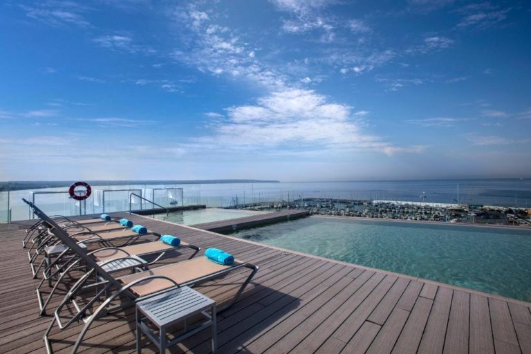 Piscina infinita con tumbonas y vistas al puerto deportivo y al mar en Hotel Las Arenas