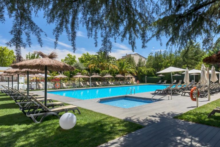 Piscina exterior con tumbonas y sombrillas del Barceló Cáceres V Centenario rodeada de jardines