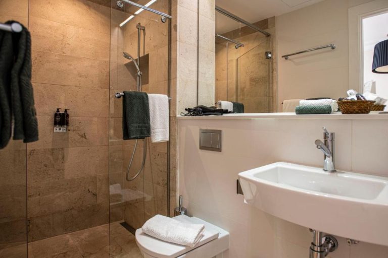 Baño moderno con ducha de mármol y lavabo en suite del hotel Palma Suites