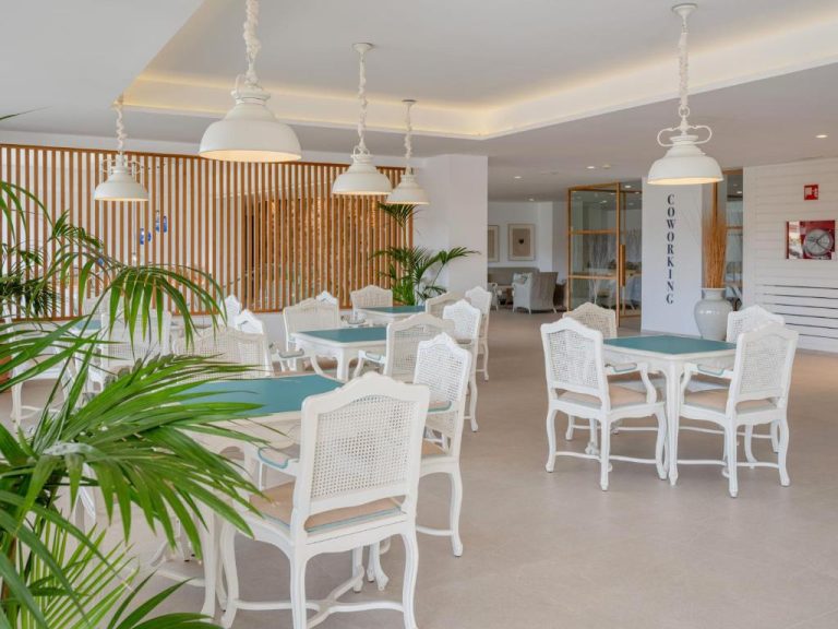 Zona de coworking con mesas y sillas blancas y plantas tropicales en el Grupotel Maritimo