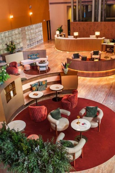 Elegante lobby lounge del Hotel Meliá Bilbao con zonas de descanso, sillones rojos y recepción circular iluminada