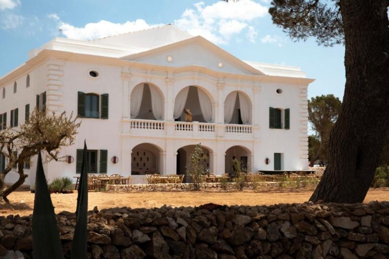 Fachada exterior blanca con arcos y terraza del Menorca Experimental rodeada de jardín y muros de piedra