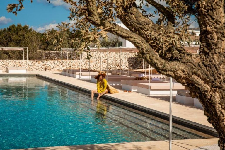 Mujer junto a la piscina exterior con solarium y tumbonas del Menorca Experimental Hotel