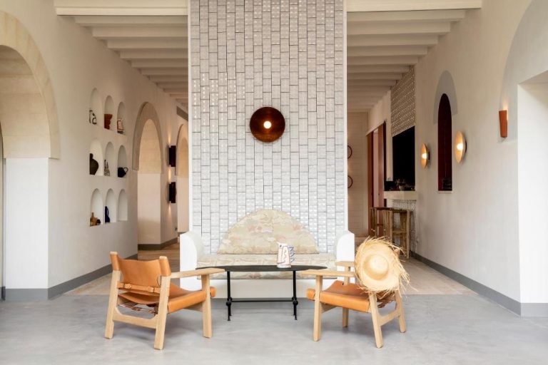 Lobby con chimenea de azulejos, sillones de cuero y arcos blancos en Menorca Experimental Hotel