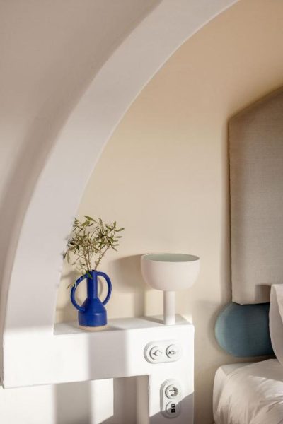 Mesita de noche con jarrón azul y lámpara blanca bajo arco en habitación del Menorca Experimental