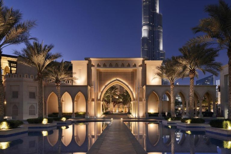 Entrada iluminada del Palace Downtown Dubai con piscina reflectante y vistas al Burj Khalifa al atardecer