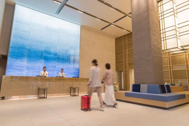 Recepción moderna del JR Kyushu Hotel Blossom Naha con viajeros y gran pantalla decorativa azul