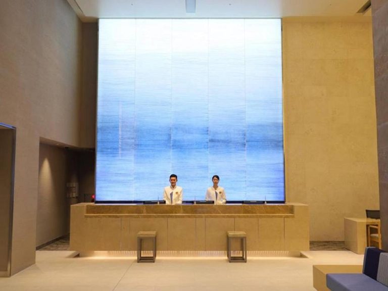 Recepción moderna con pantalla luminosa azul y personal en el JR Kyushu Hotel Blossom Naha