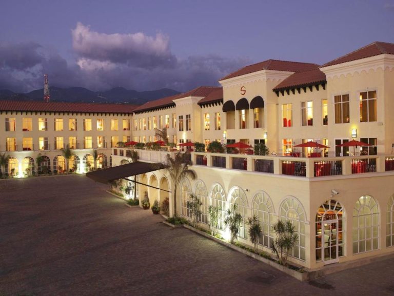 Fachada exterior iluminada del S Hotel Kingston al atardecer con terraza y montañas al fondo