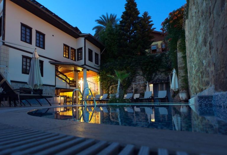 Piscina exterior iluminada de noche en el Dogan Hotel con tumbonas y edificio histórico de fondo