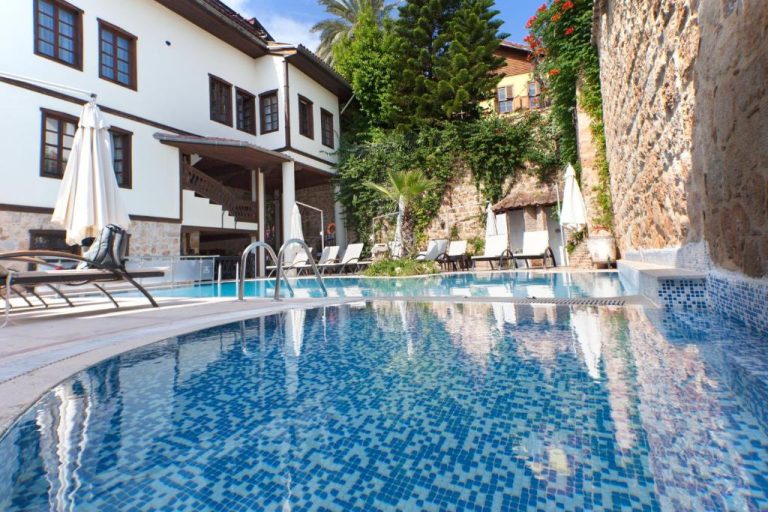 Piscina exterior del Dogan Hotel rodeada de tumbonas y muros de piedra históricos en Antalya