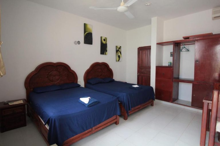 Habitación doble con camas de madera tallada y ropa de cama azul en Villas Roseliz