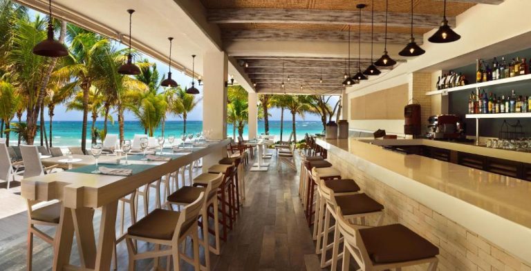 Restaurante bar con vistas al mar turquesa y palmeras en Catalonia Royal Tulum Beach & Spa Resort