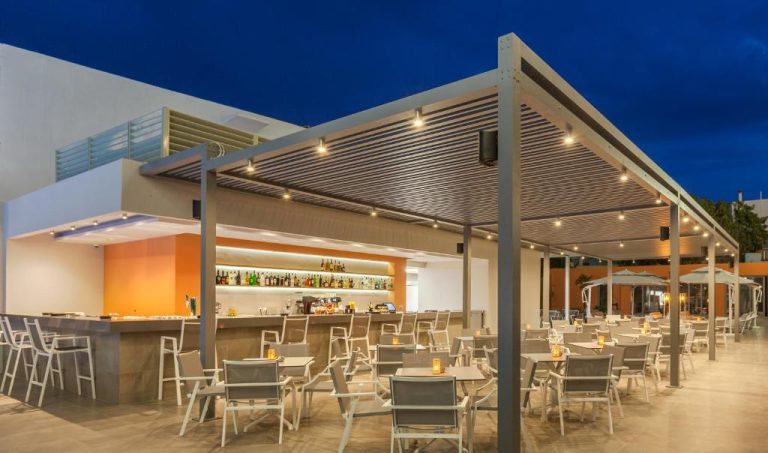 Terraza bar exterior iluminada del Blue Lagoon City Hotel con mesas y barra de cócteles al atardecer