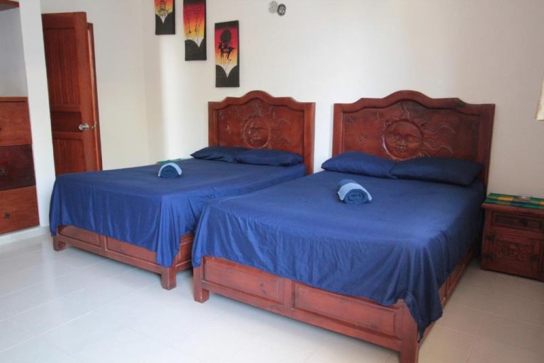 Habitación doble con camas talladas en madera y ropa de cama azul en Villas Roseliz