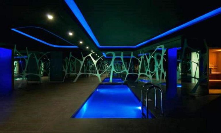 Piscina interior iluminada con luces azules y decoración moderna en A Point Arezzo Park Hotel