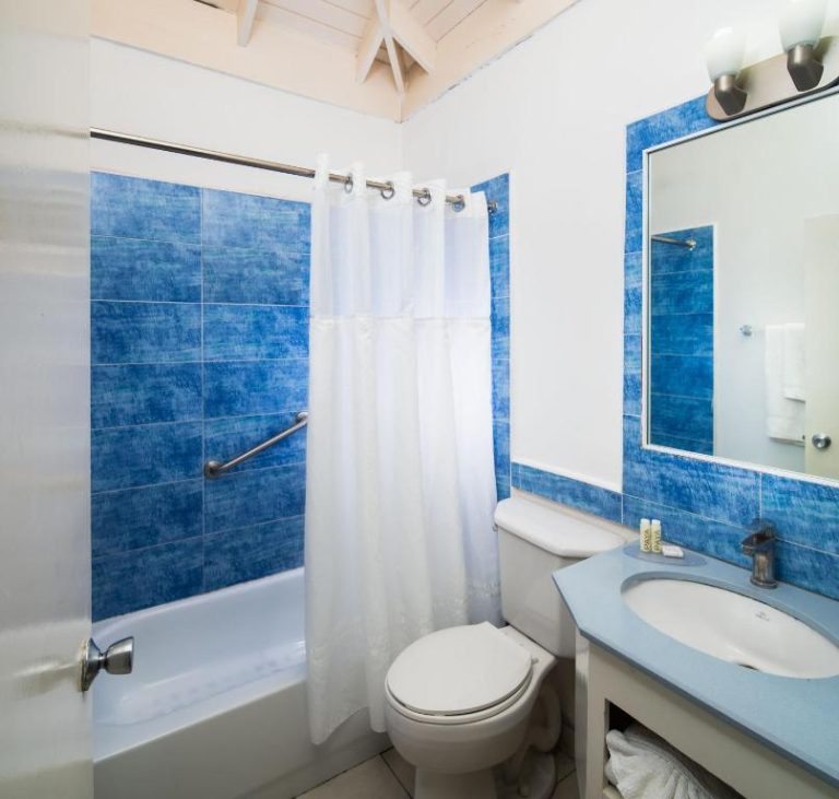 Baño con azulejos azules, bañera con cortina blanca y lavabo del Deja Resort All Inclusive