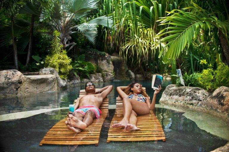 Pareja relajándose en tumbonas flotantes junto a la piscina tropical de Sweetfield Manor