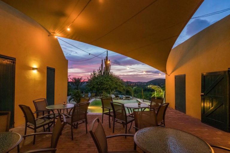 Terraza exterior con mesas y sillas del Landhuis Klein Santa Martha Boutique Hotel con vista a la piscina al atardecer