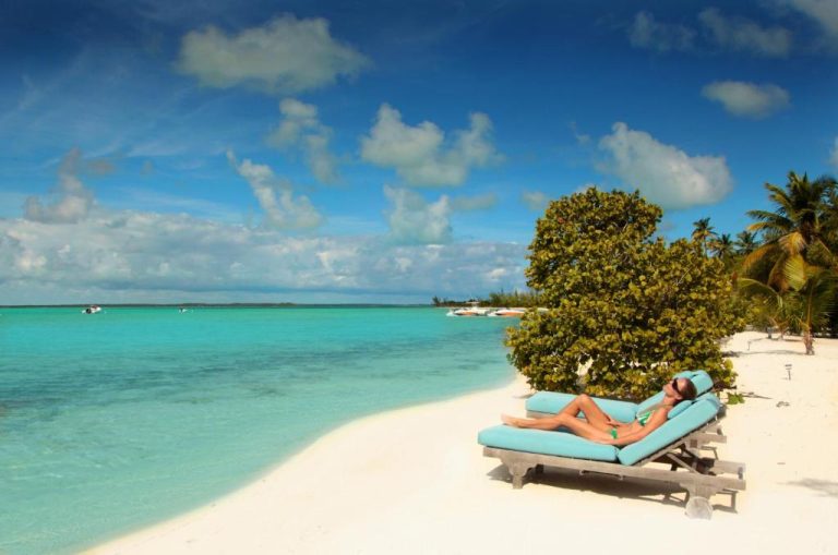 Turista relajándose en tumbona azul en la playa privada de aguas turquesas del Tiamo Resort