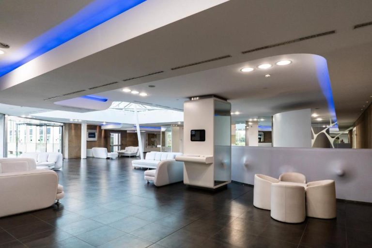 Lobby moderno con sofás blancos e iluminación azul del A Point Arezzo Park Hotel