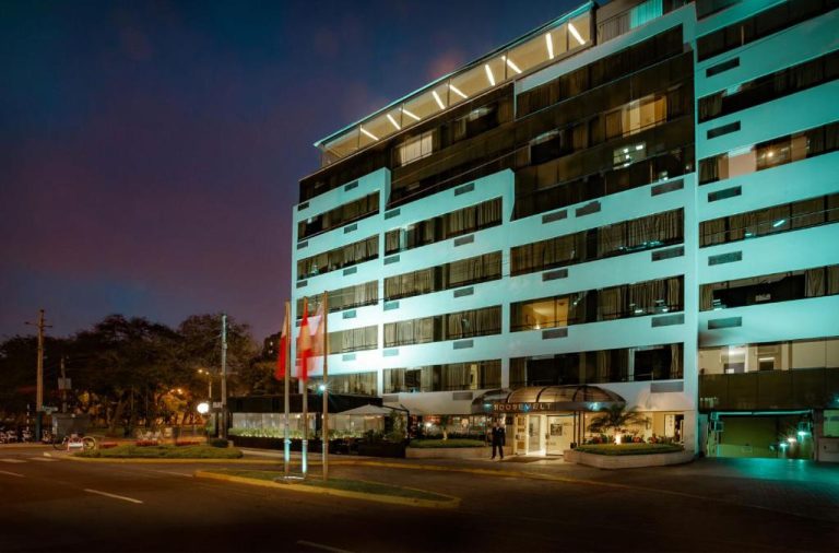 Fachada iluminada del Roosevelt Hotel & Suites de noche con vista a la avenida principal