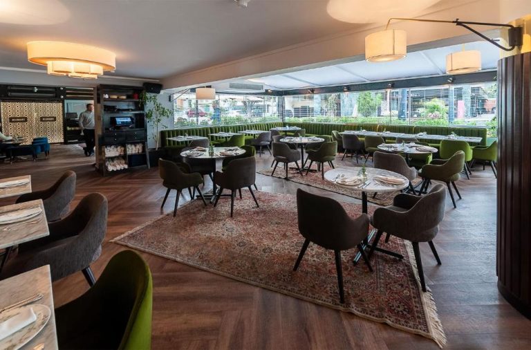 Elegante restaurante interior del Roosevelt Hotel & Suites con sillas verdes y mesas dispuestas sobre alfombras