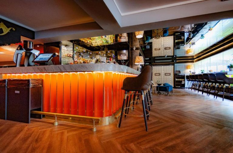 Barra de bar con iluminación naranja y taburetes en el Roosevelt Hotel & Suites