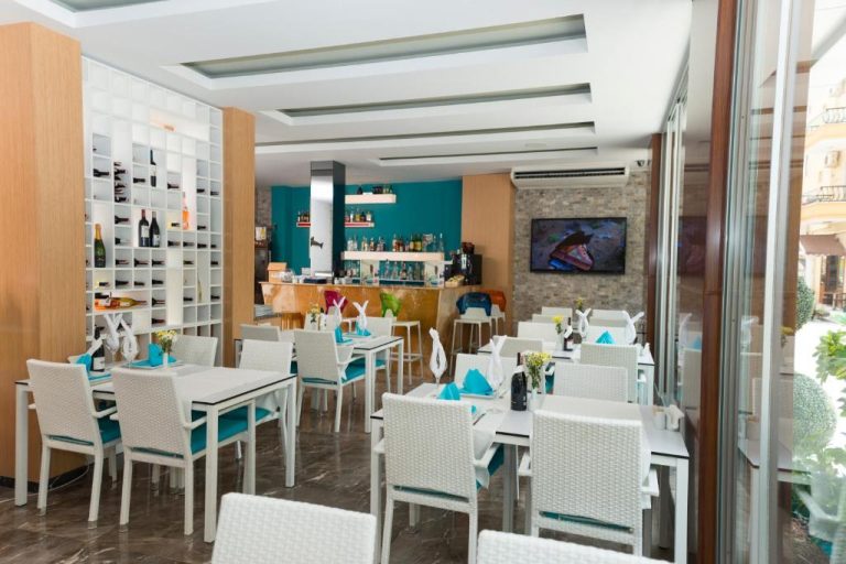 Restaurante y bar del Kleopatra Suit Hotel con mesas blancas, sillas turquesa y bodega de vinos