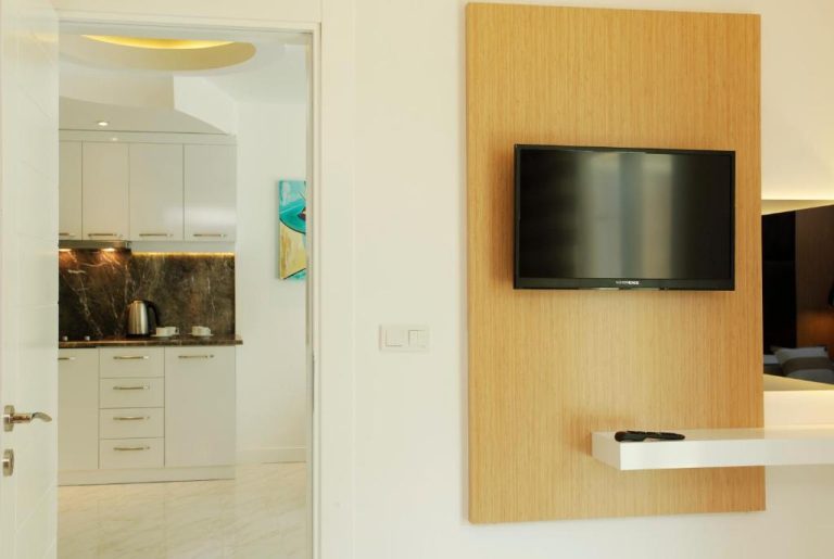Salón con televisión empotrada en panel de madera y cocina equipada del Kleopatra Suit Hotel
