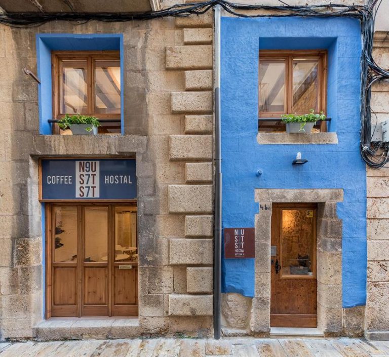 Fachada exterior del Hostal 977 con café integrado, piedra natural y pared azul en el casco antiguo