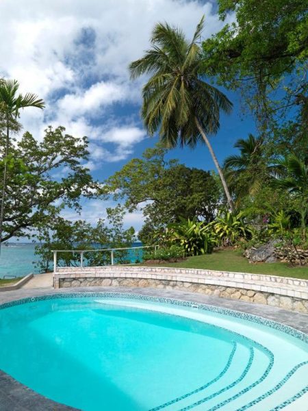 Piscina exterior con vistas al mar turquesa rodeada de palmeras tropicales en Jamaica Inn