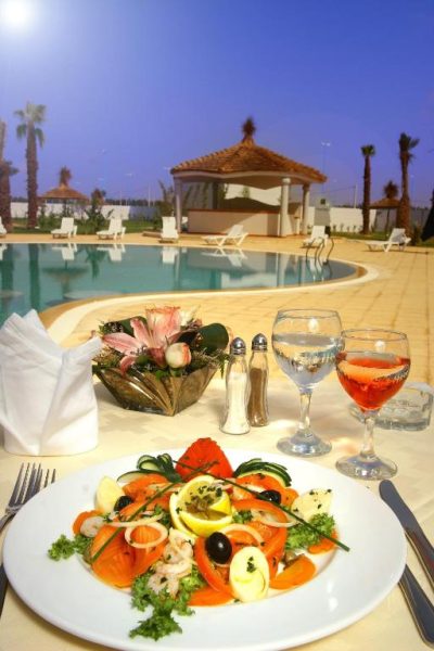 Cena romántica junto a la piscina exterior del Relax Hotel Airport Nouasseur con ensalada y copa de vino