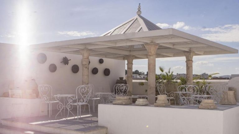 Terraza exterior con pérgola de estilo árabe y sillas de hierro blancas en Dar Ben Gacem Kahia