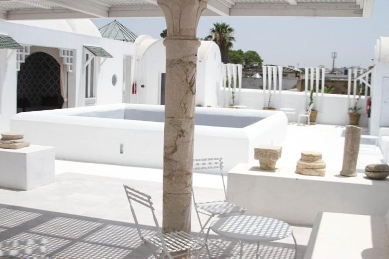 Terraza blanca con columnas de piedra y piscina exterior del Dar Ben Gacem Kahia en Túnez