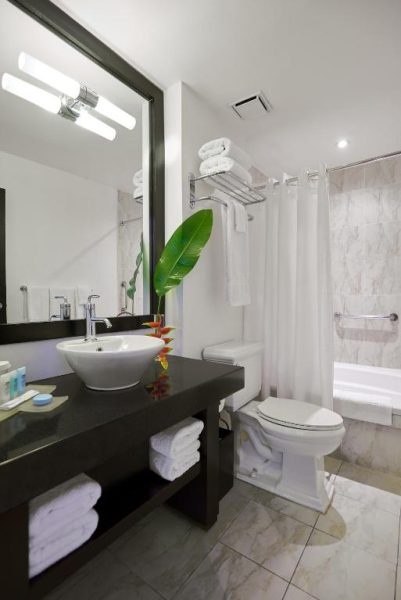 Baño moderno con bañera y ducha del S Hotel Kingston, decorado con toallas blancas y planta tropical