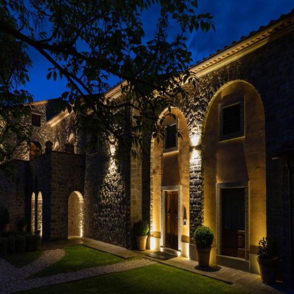 Fachada de piedra iluminada con arcos del Relais La Corte dei Papi durante la noche