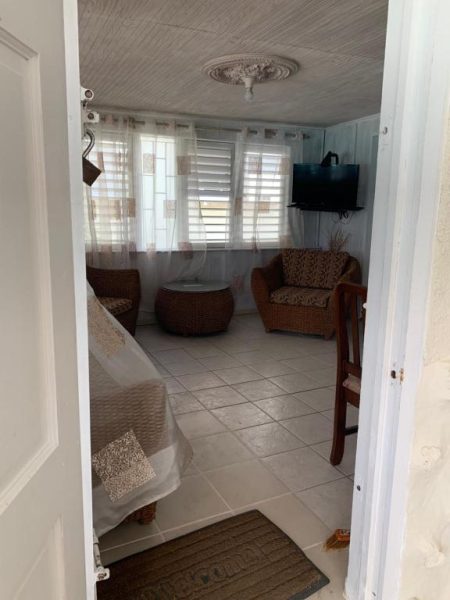 Sala de estar con sillones de mimbre y TV en Beach Vue Barbados con suelo de baldosas blancas