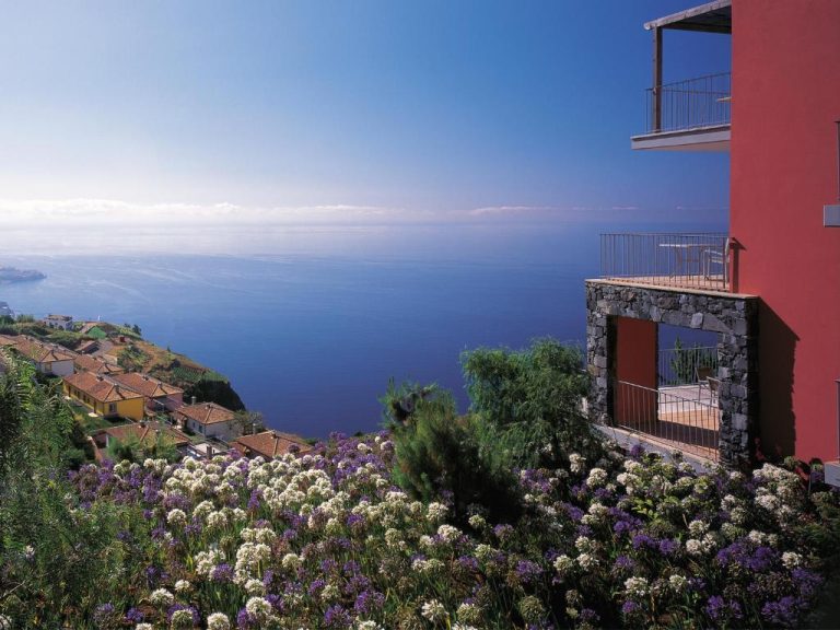 Vistas panorámicas al océano desde Village Cabo Girão con jardines de flores y casas en la ladera