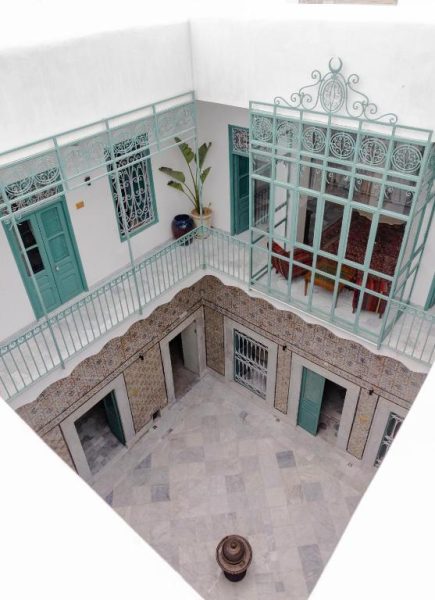 Patio interior tradicional árabe con balcones de forja turquesa y azulejos en Dar Ben Gacem Kahia