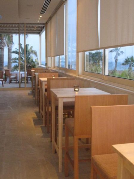 Restaurante con mesas de madera y vistas panorámicas al mar en E-Hotel Larnaca Resort & Spa