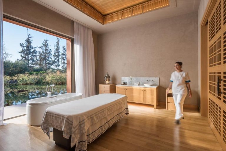 Sala de tratamientos spa con camilla y bañera exenta con vistas al jardín en The Oberoi Marrakech