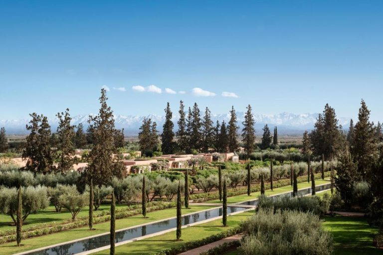 Jardines con canales de agua y cipreses del The Oberoi Marrakech con las nevadas montañas del Atlas al fondo