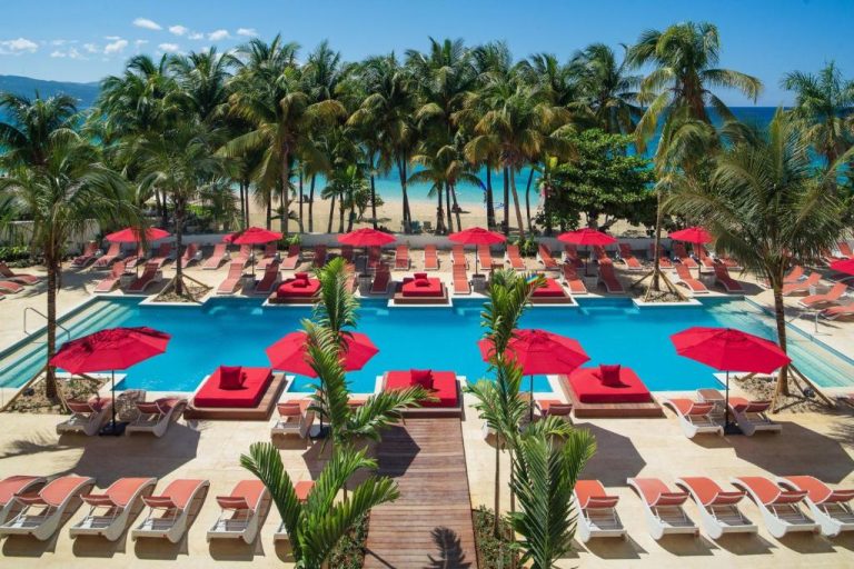Piscina exterior con tumbonas rojas y sombrillas del S Hotel Montego Bay frente a la playa de Jamaica
