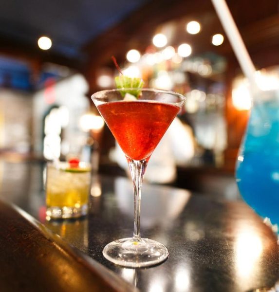 Cócteles coloridos sobre la barra del bar del Courtleigh Hotel & Suites, incluyendo un martini rojo y bebida azul