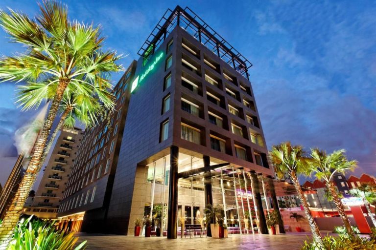 Fachada exterior nocturna del Holiday Inn Santo Domingo by IHG con palmeras y entrada iluminada