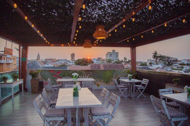 Terraza rooftop con mesas de madera y vistas al atardecer sobre la ciudad en Cartagena Royal Hotel Boutique