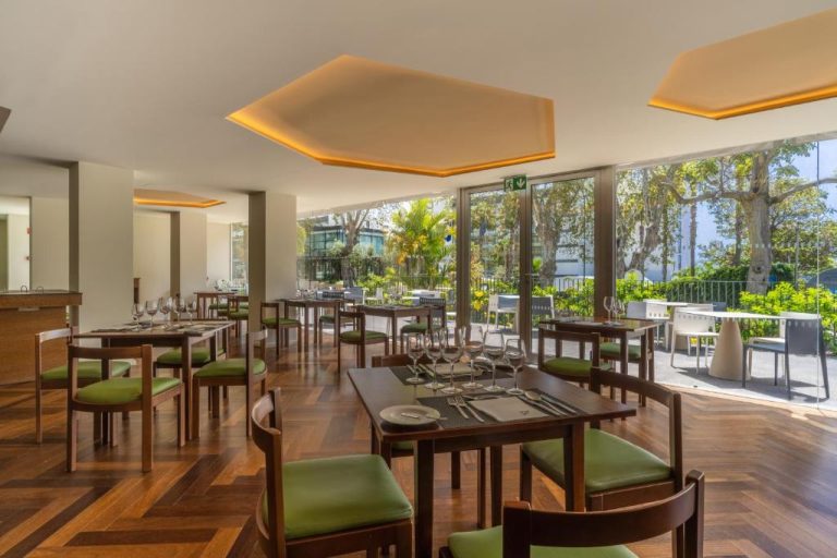 Restaurante interior del Hotel Girassol Suite Hotel con sillas verdes y vistas al jardín exterior